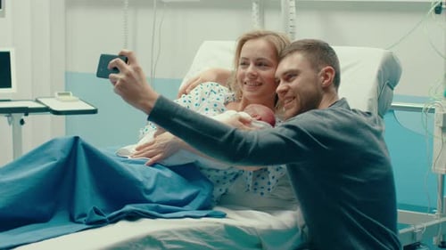 Father Takes Selfie of Him with His Wife Holding Newborn Baby while Lying on the Hospital Bed. Happ