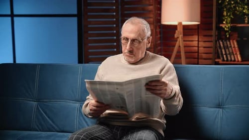 Man Reading Newspaper While Sitting on Couch