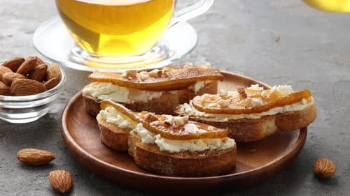 Woman dripping honey onto delicious bruschetta with cream cheese, pear and almonds at grey table