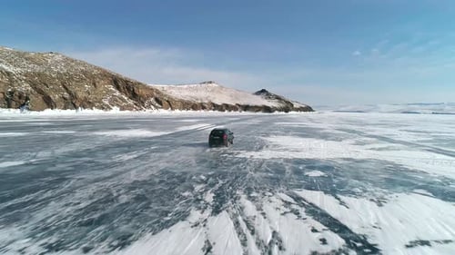 Aerial View on a Car Driving on Cracked Ice of Baikal to the Famous Tourist Spot Winter Landscape of