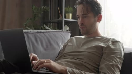 Man Works on Laptop at Home on Sofa