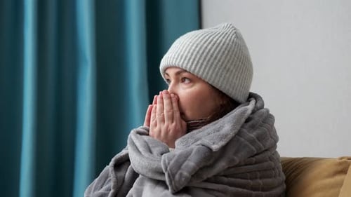 Une femme adulte se couvre d'une couverture et essaie de se réchauffer à la maison