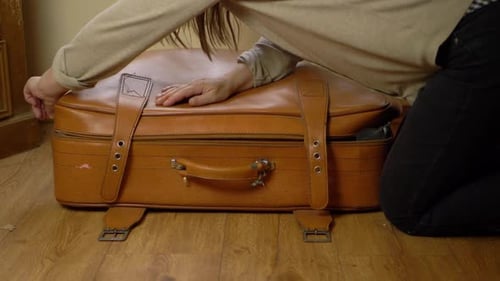 Woman packing large vintage suitcase on wooden floor