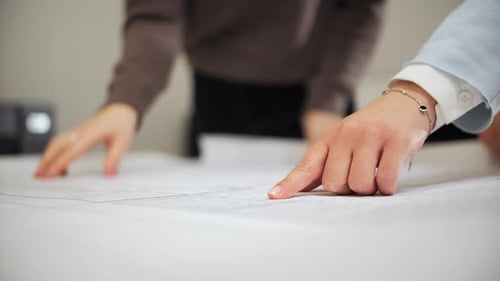 Hands Pointing at Architectural Plans in Office