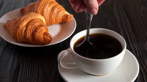 Coffee Being Stirred Next to Croissants on Dark Table