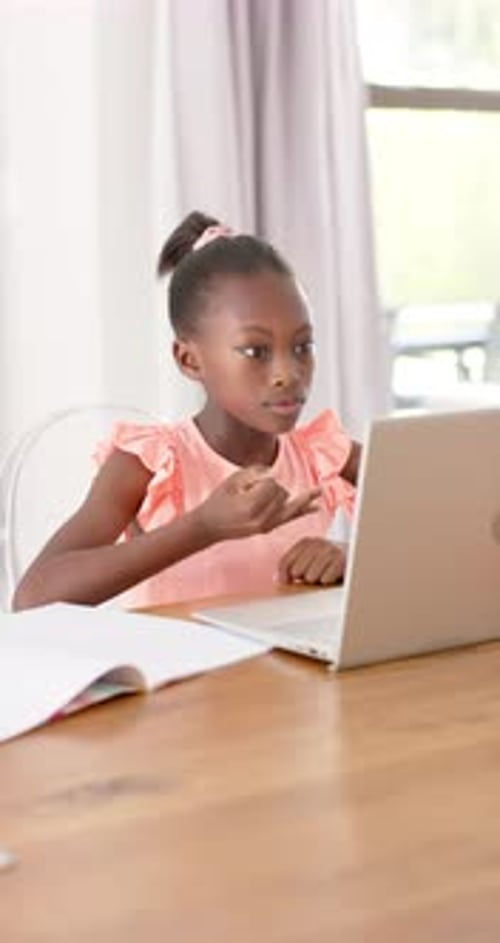 Vertical video: African child in pink top watching laptop lesson, counting on fingers with notebook
