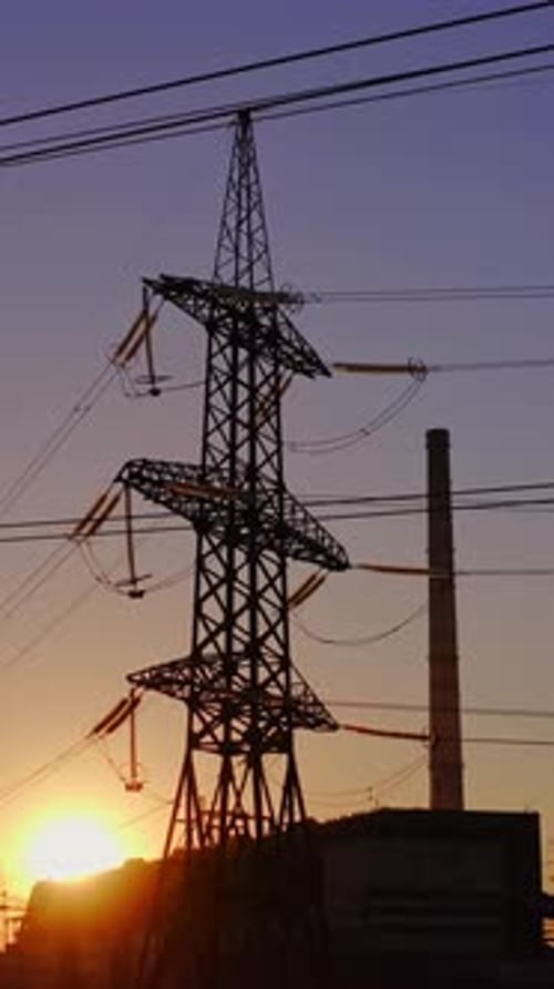 Electricity pylons and lines at dusk. Silhouette of high voltage tower and wires. Vertical video