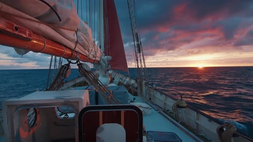 Sailing expedition boat moves in the open sea during bright pink sunrise