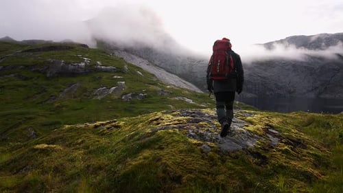 Young Man Standing at Famous Cliff Edge and Enjoying a Scenic View Over a Valley Lake and the