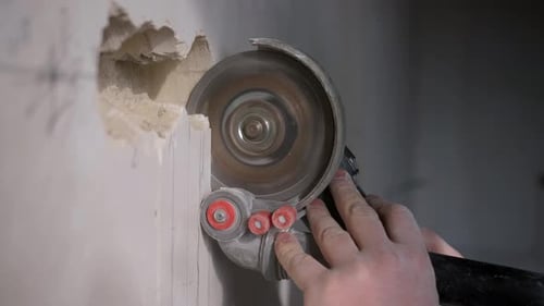 A Man Uses a Grinder to Make Holes in the Wall for Electrical Wiring