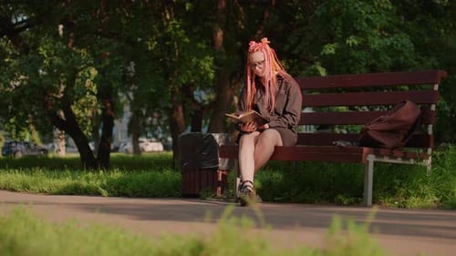 Young Woman Reads Book on Park Bench