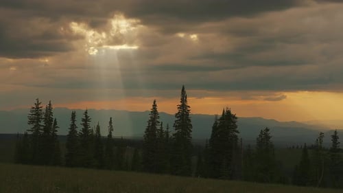 Sunrays Behind Clouds Across Mountain Trees. Time-lapse, Pan Right Shot