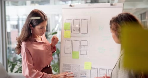 Two Women Discuss App Wireframes in Office