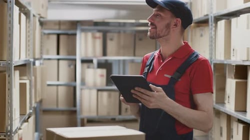 Warehouse Worker Uses Digital Tablet For Checking Stock, On the Shelves Standing Cardboard Boxes, P