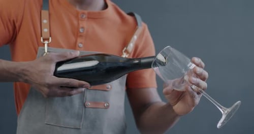 Closeup of Male Hand Pouring Red Wine in Glass and Giving to Camera on Gray Color Background