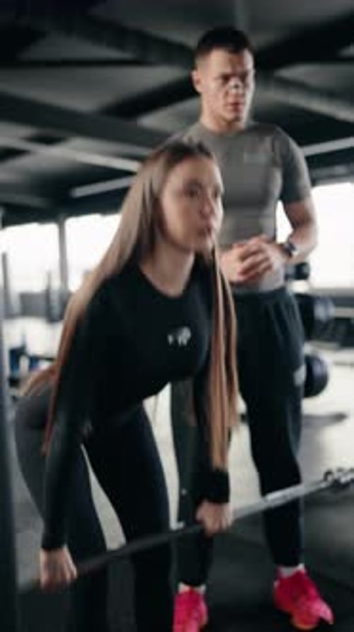 Woman Deadlifts with Barbell Guided By Personal Trainer in Gym
