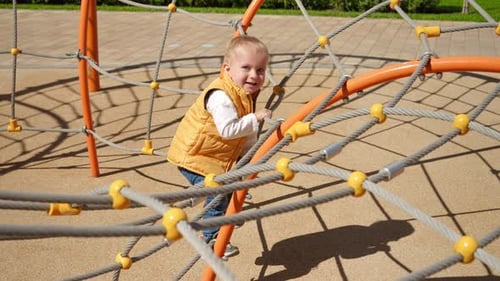 Little baby boy climbing up the spider web on playground