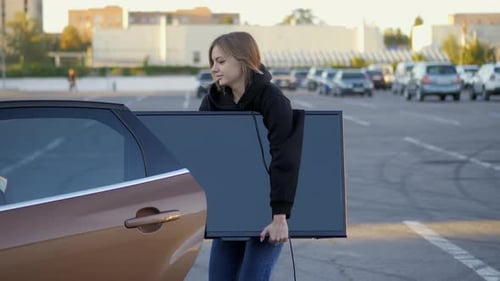 Woman Funny Trying to Put Purchased Modern Tv in Car Trunk at Store Parking in Closeup