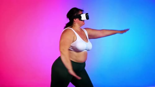 Woman with overweight in a tracksuit and VR headset doing exercises in a studio with blue and red ba