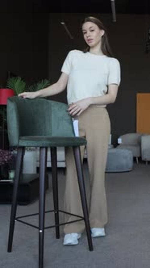 Young Woman Choosing a Bar Stool in a Furniture Store