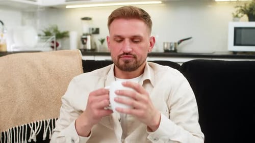 Man Relaxes on Sofa and Drinks Coffee