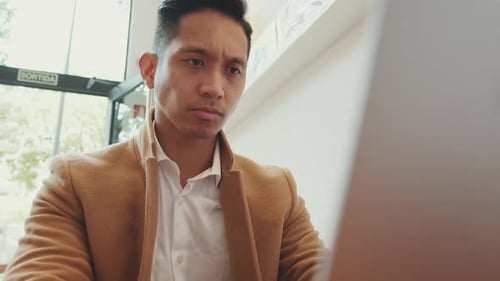 Close-up of young businessman wearing beige suite working with laptop in cafe