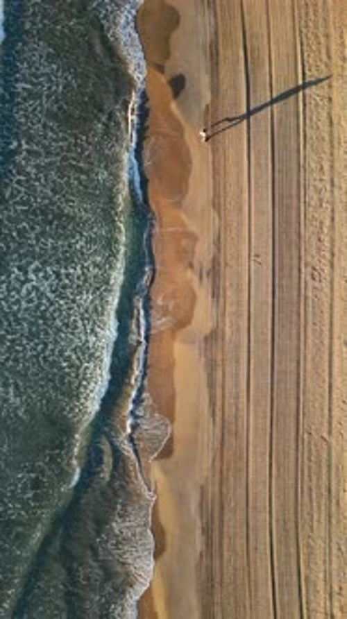 Man walking on the beach with waves hitting the shore in Alicante, Spain. Vertical