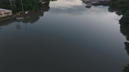 Forwards Fly Above Calm Water Surface Mirroring Sky Tilt Up Reveal Buildings and Vegetation Along
