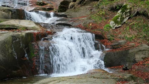 Mountain stream waterfall flowing over rocks in autumn forest