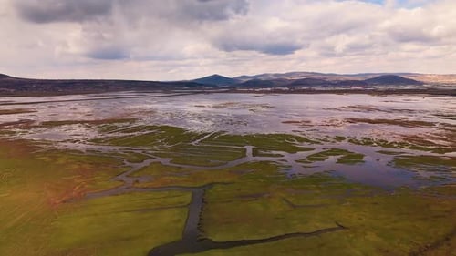 Dramatic reflection of white clouds on a calm wetland surface with distant mount