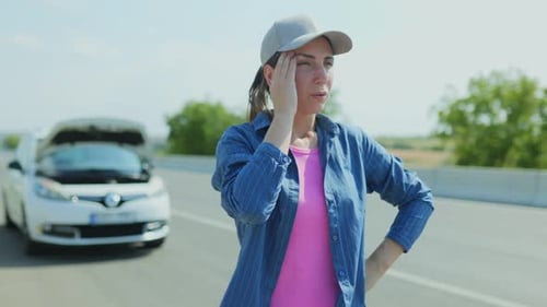 Frustrated Young Woman Stands Beside Broken Car on Highway