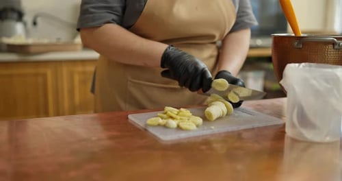 Closeup of a Girl Baker in Black Rubber Gloves Cuts Bananas for Preparing Dessert in a Bakery Cafe