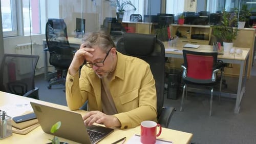 Müder männlicher Manager, der im Büro am Laptop arbeitet
