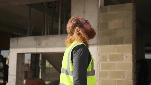Overworked builder worker during break inspects brick wall under construction