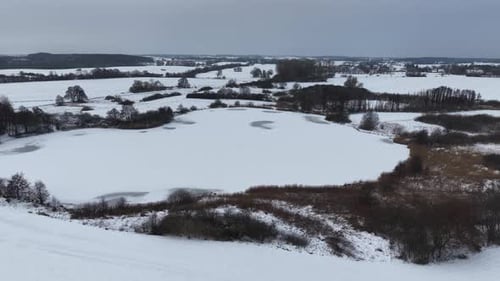 Aerial drone footage flying over a frozen lake and snow-covered countryside during winter. The