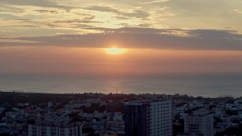 Aerial shot capturing sunn getting covered by thick clouds at horizon with cityscape in foreground.