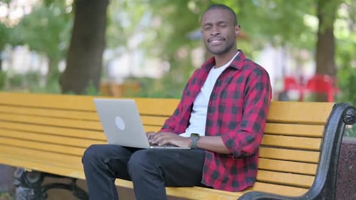 Man Laughing While Using Laptop on Park Bench