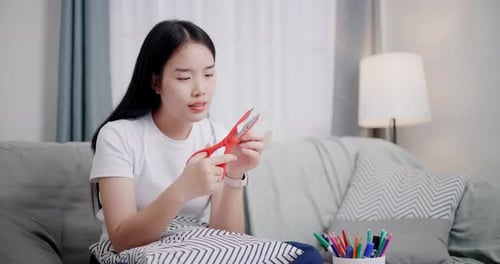 Young Woman Cutting Paper with Scissors at Home