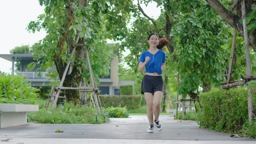 Young asian woman runner wearing headphones to listen to music while running in park.