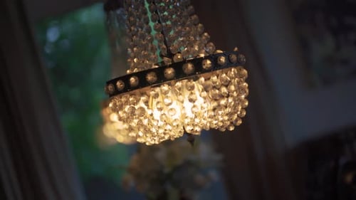 Ein Kristall-Kronleuchter, der von der Decke hängt und auf den warmes Licht scheint.