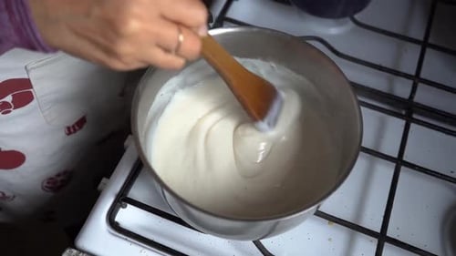 Hand Cooking And Stirring Bechamel Sauce In A Sauce Pan Over The Stove. overhead