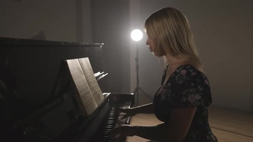 Female pianist learning new piano music part, alone on studio with heir light background