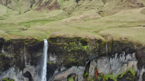 Drone Of Waterfall Flowing Over Cliff From Green Landscape