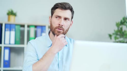 Nahaufnahme eines nachdenklich denkenden gutaussehenden bärtigen Mannes vor einem Laptop-Computerbildschirm