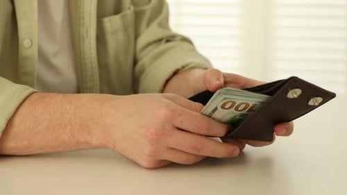 Homme sortant des billets en dollars du portefeuille et comptant à la table blanche, gros plan