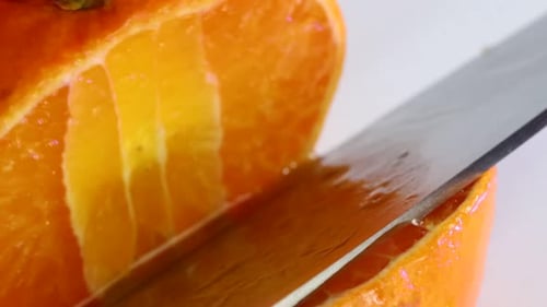 Very sharp knife cutting a thic slice of tangerine. Chopping, slicing, close up macro shot.