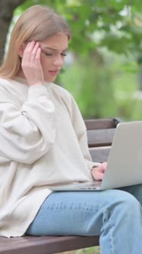 Woman Sitting on Bench Experiencing Headache Using Laptop
