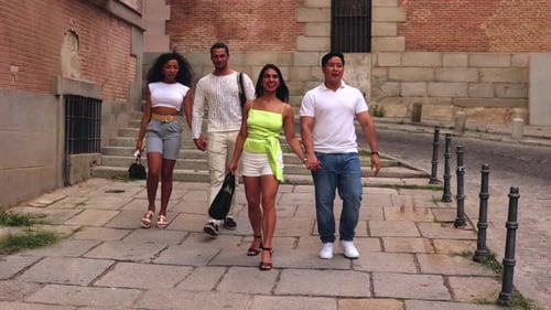 Group of four multiethnic friends walking and holding hands on a historic cobblestone street. Two ha