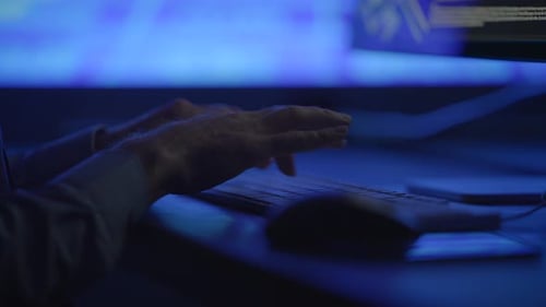 A CloseUp of Hands Actively Typing on a Computer Keyboard in a Dimly Lit Room Environment