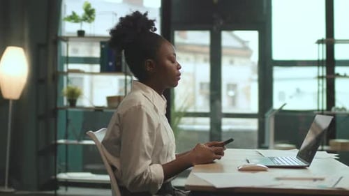 African American Business Woman Sitting on Chair Use Phone and Laptop Work in Office Serious Camera
